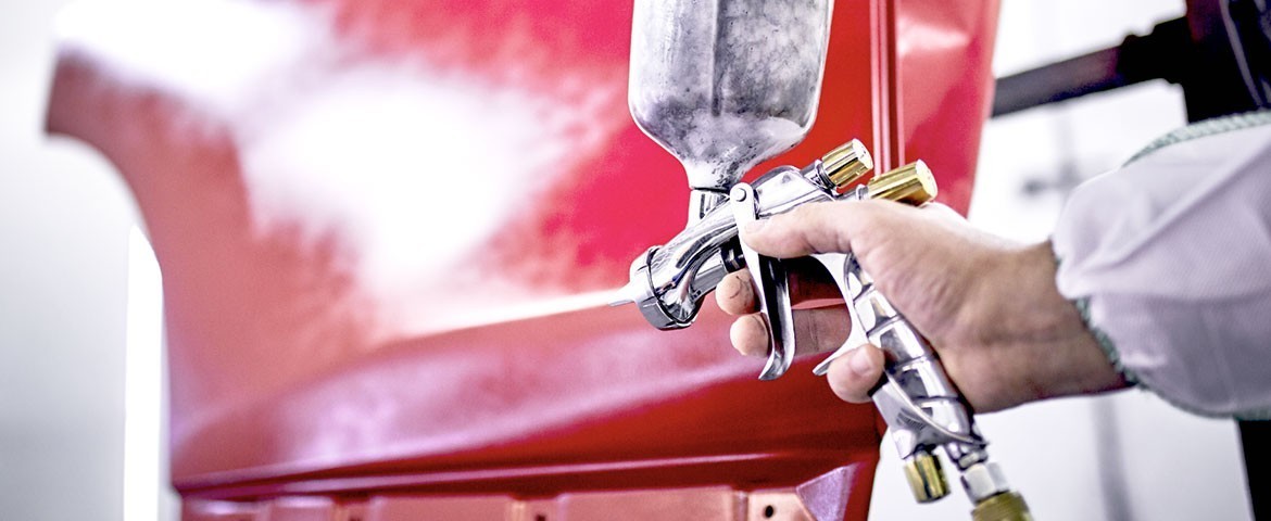 Main vaporisant un produit sur une voiture rouge