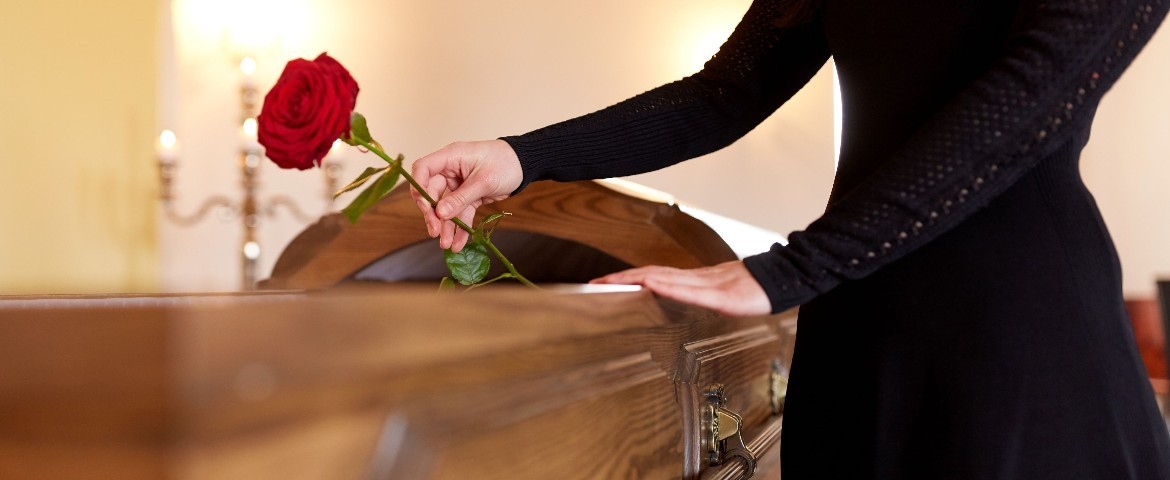 Femme en robe noire qui dépose une rose rouge dans un cercueil en bois.