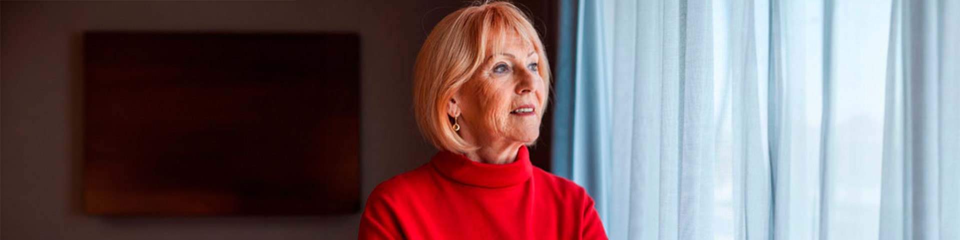 femme au pull rouge regardant par la fenêtre