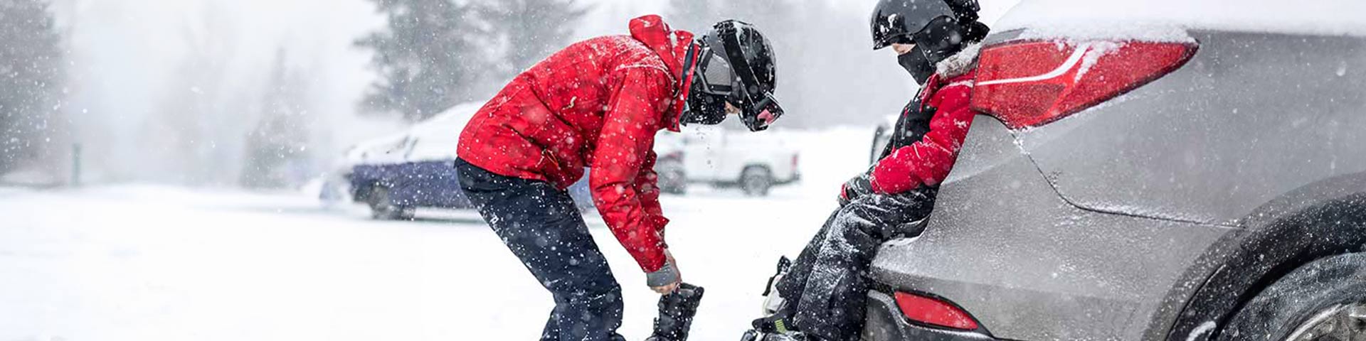 Deux personnes qui se préparent pour skier sur un parking enneigé 