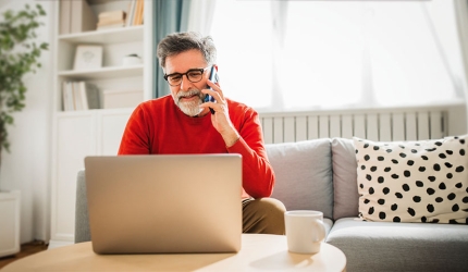 Un homme au téléphone consultant son ordinateur assis sur son canapé