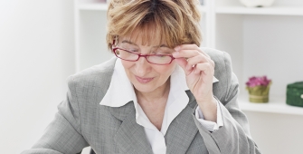 Une femme en costume gris tient ses lunettes pour lire