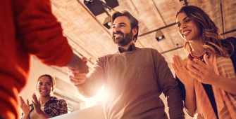 Deux personnes qui se serrent la main, entourées de personnes qui les applaudissent 