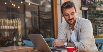 Un homme assis à la terrasse d'un bar avec son ordinateur