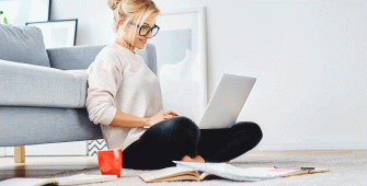 Une femme assise en tailleur au pied de son canapé avec l'ordinateur sur ses genoux