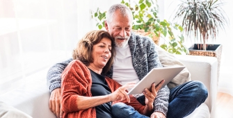 Un couple âgé sur un canapé qui regarde leur tablette 
