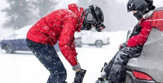 Deux personnes qui se préparent pour skier sur un parking enneigé 