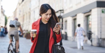 Une femme  dans la rue avec son téléphone et un café dans la main 