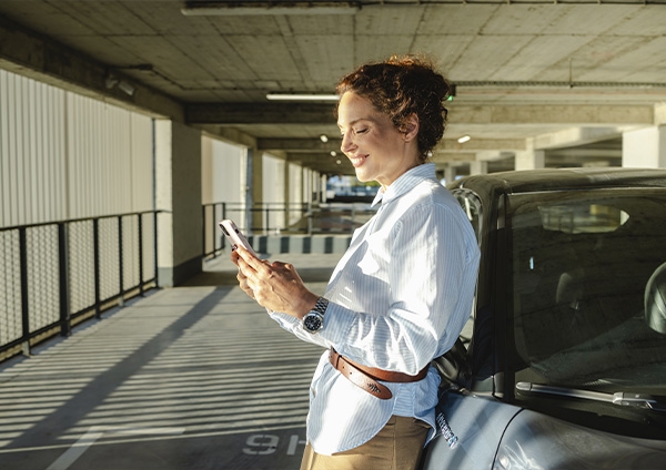 Une femme devant sa voiture qui regarde son téléphone